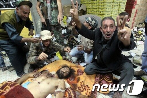 본문 이미지 - 20일(현지시간) 시르테에서 숨진 뒤 미스라타로 옮겨진 무타심의 시신 앞에서 사람들이 승리의 V자 표시를 하고 있다. AFP © News1