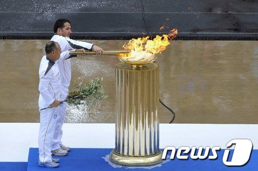 본문 이미지 - 17일(현지시간) 그리스 아테네 올림픽 스타디움에서 열린 런던 올림픽 성화 전달식에서 그리스의 마지막 주자인 '역도 영웅' 피로스 디마스와 중국 체조 스타 리닝이 성화대에 성화를 옮기고 있다. © AFP=News1 
