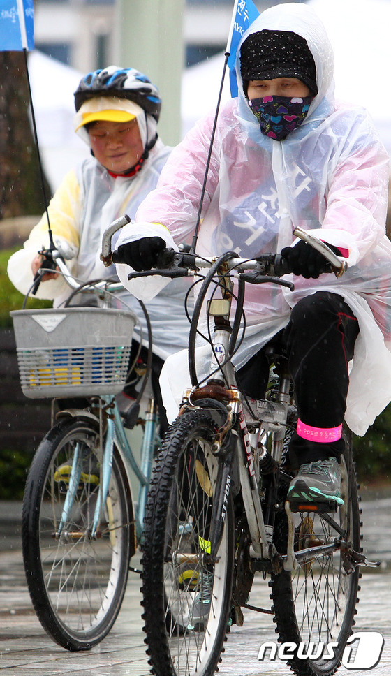 (전주=뉴스1) 김대웅 기자 = 27일 전북도청 앞 광장에서 열린 친환경 녹색교통수단 자전거 타기 대행진에 참석한 시민들이 갑자기 내린 소나기를 피하기 위해 우비를 입고 자전거를 …