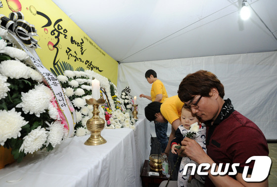 (전주=뉴스1) 김대웅 기자 = 故 노무현 전 대통령 서거 4주기 추도식이 열린 23일 전북 전주오거리문화광장에 마련된 분향소에서 한 시민이 아이를 안고 헌화를 하고 있다. 201 …