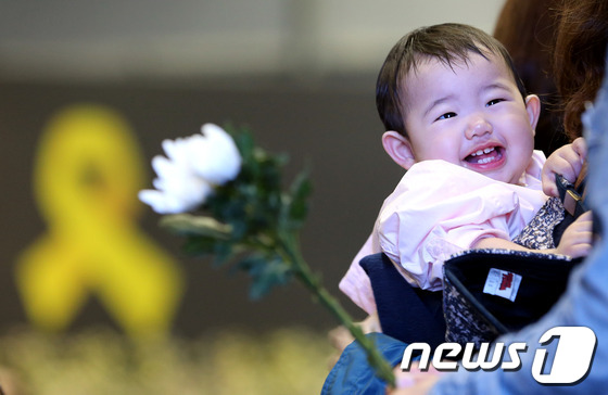 (안산=뉴스1) 사진공동취재단 = 2일 오후 경기도 안산 세월호 침몰사고 희생자 정부합동분향소에서 한 아기가 국화꽃 옆에서 환한 미소를 보이고 있다. 2014.5.2/뉴스1