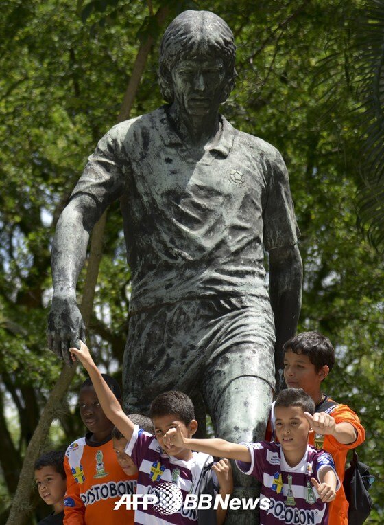 본문 이미지 - 콜롬비아 축구 꿈나무들이 3일(한국시간) 안드레스 에스코바르의 동상에서 밝게 웃고 있다.  한 소년은 에스코바르의 손을 꼭 잡고 있다. © News1 