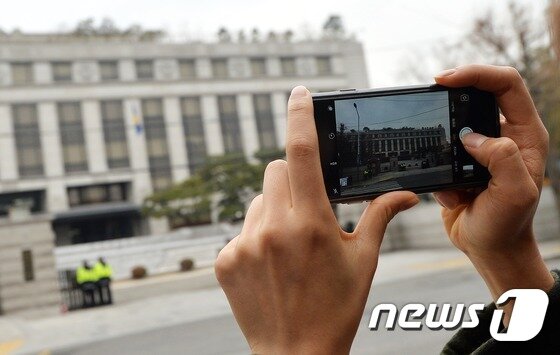 본문 이미지 - 서울 종로구 재동 헌법재판소 앞에서 한 여성이 청사 전경을 휴대폰 카메라에 담고 있다. 2016.12.18 ⓒ 뉴스1 오대일 기자