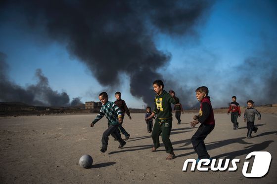 본문 이미지 - 아이들이 지난달 20일(현지시간) 알콰야라 마을에서 시커먼 유전 연기가 하늘을 뒤덮는 가운데 축구를 즐기고 있다. ⓒ AFP=뉴스1