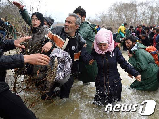 본문 이미지 - 난민들이 지난 3월 그리스-마케도니아 국경을 넘기 위해 진흙 섞인 강을 건너고 있다. 누라 역시 이 같은 열악한 상황을 겪었다. ⓒ AFP=뉴스1