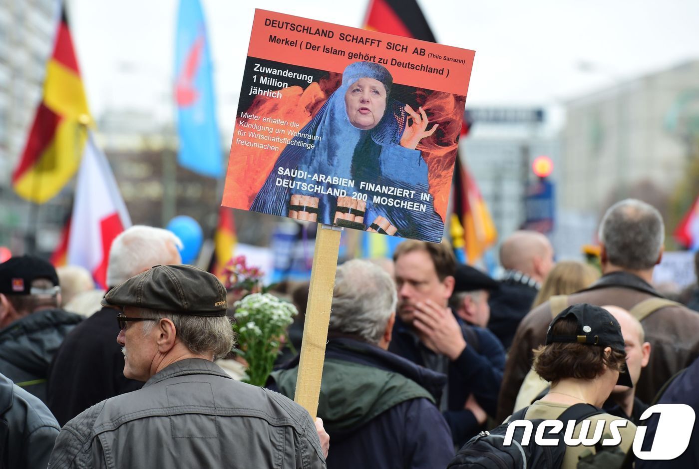 본문 이미지 - 반(反)이민을 주장하는 독일 극우 정당 '독일을 위한 대안'(AfD) 지지자가 무슬림 복장인 '부르카'를 두른 앙겔라 메르켈 총리의 합성사진을 들고 있다. ⓒ AFP=뉴스1