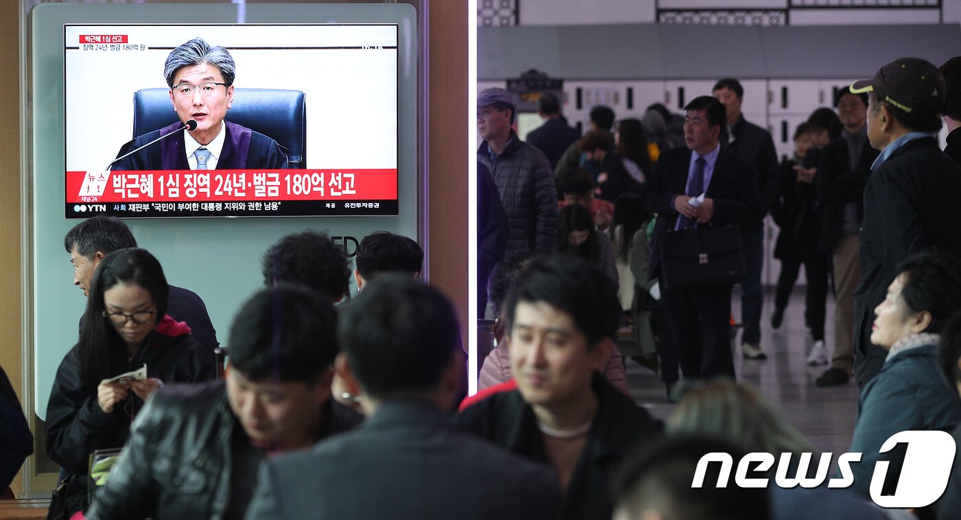 본문 이미지 - 4월 6일 오후 서울 용산구 서울역 대합실에서 시민들이 박근혜 전 대통령의 1심 선고 공판 생중계를 보고 있다. 이날 김세윤 서울중앙지법 부장판사는 미르·K스포츠재단 출연금을 대기업에 강제하는 등 18개 혐의로 구속기소된 박 전 대통령에게 징역 24년과 벌금 180억원을 선고했다. 2018.4.6/뉴스1 ⓒ News1 신웅수 기자