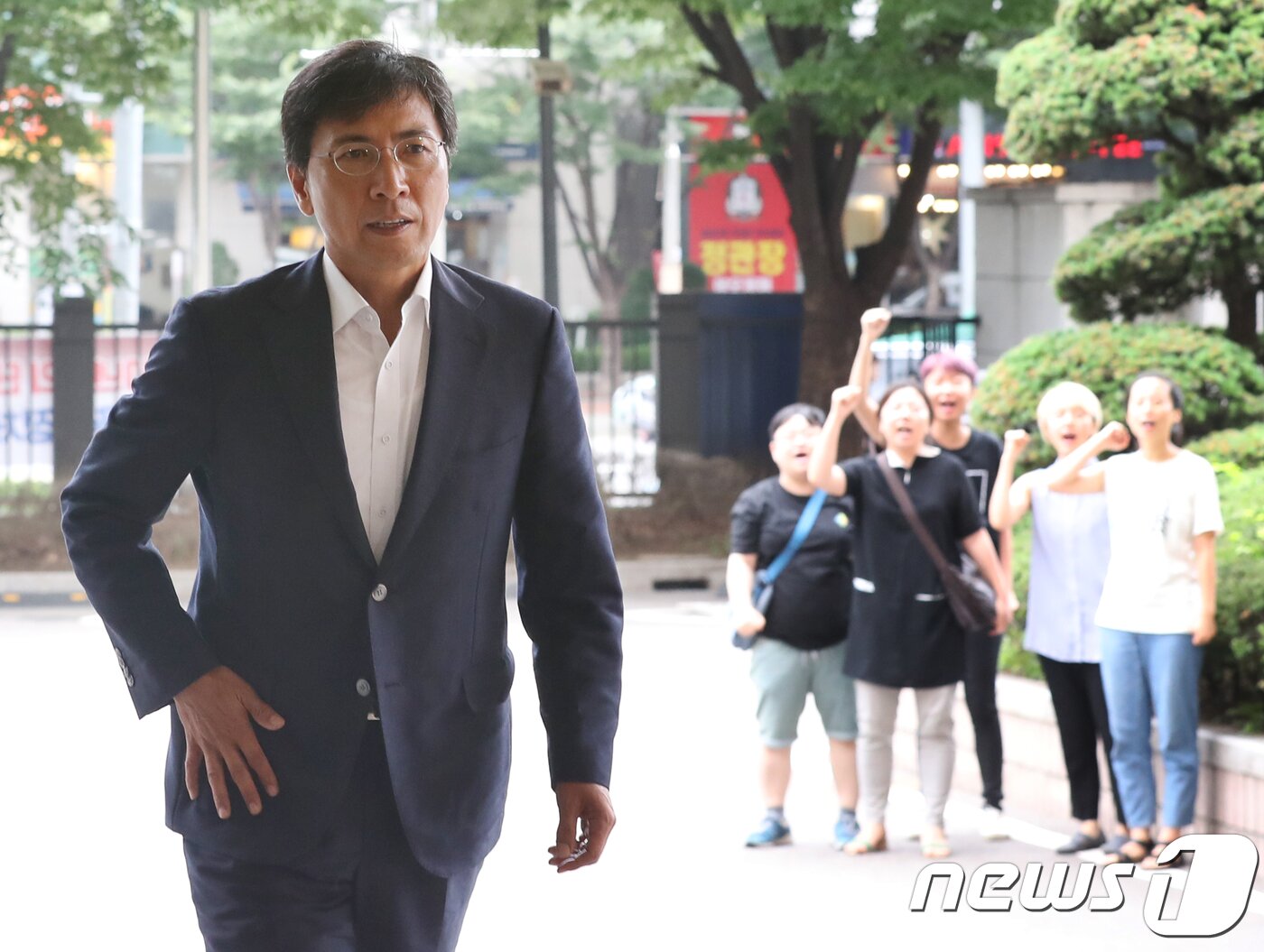 본문 이미지 - 수행비서를 위력으로 성폭행한 혐의 등을 받는 안희정 전 충남지사가 13일 오전 서울 마포구 서부지방법원에서 열린 5차 공판에 출석하고 있다. 안 전 지사 뒤에서 전국성폭력상담소협의회 등 회원들이 '증인 역고소'에 항의하며 구호를 외치고 있다. 2018.7.13/뉴스1 ⓒ News1 송원영 기자