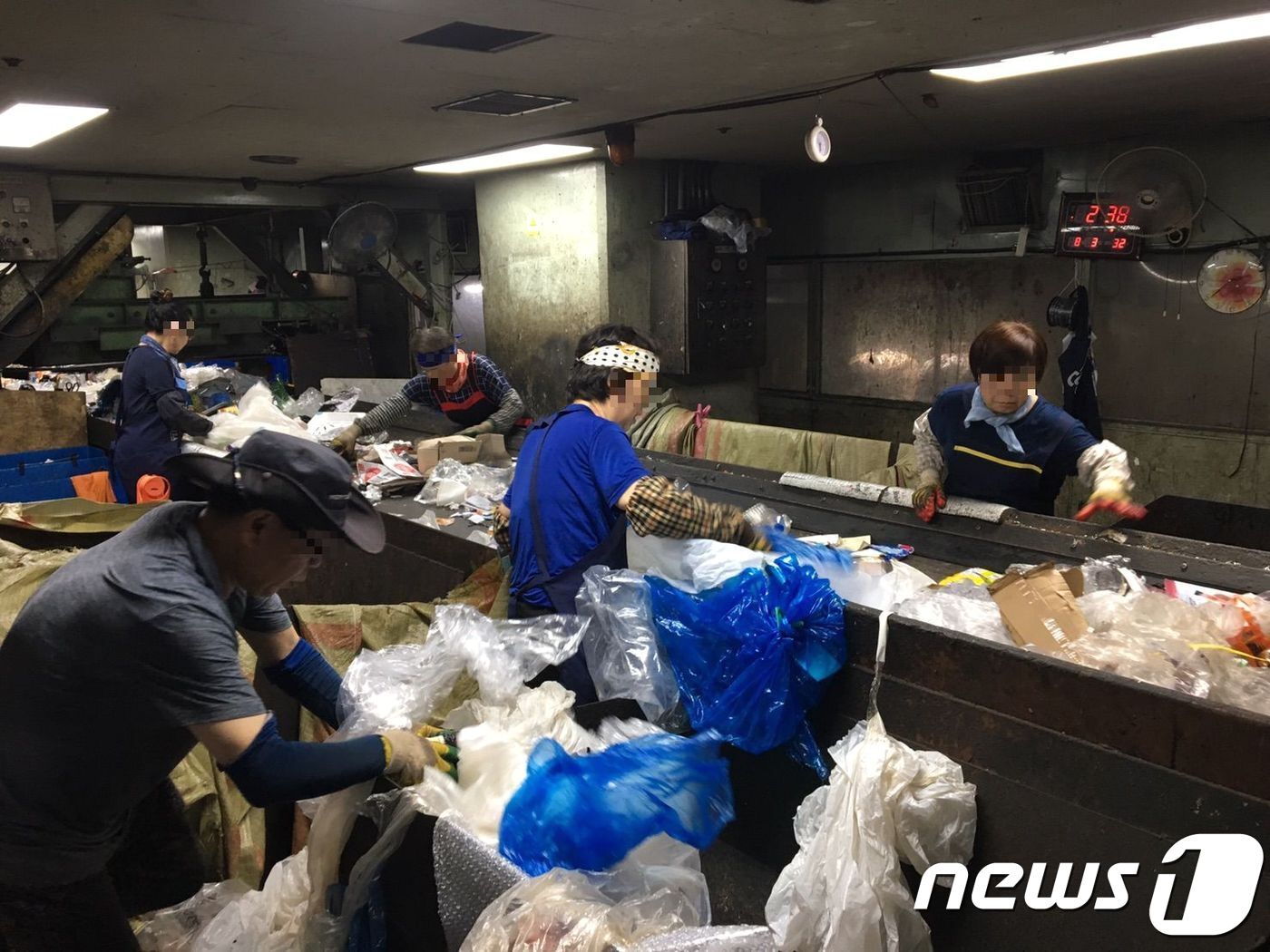 본문 이미지 - 재활용선별장에서 작업자들이 쓰레기를 손으로 선별하고 있다. 벨트 위로는 음식물이 섞인 쓰레기가 수시로 쏟아졌다. 에어컨이 가동되고 있었지만 작업장 벽면에 나타난 전광판은 실내온도 32도를 가리키고 있었다.2018.8.7/뉴스1ⓒ News1