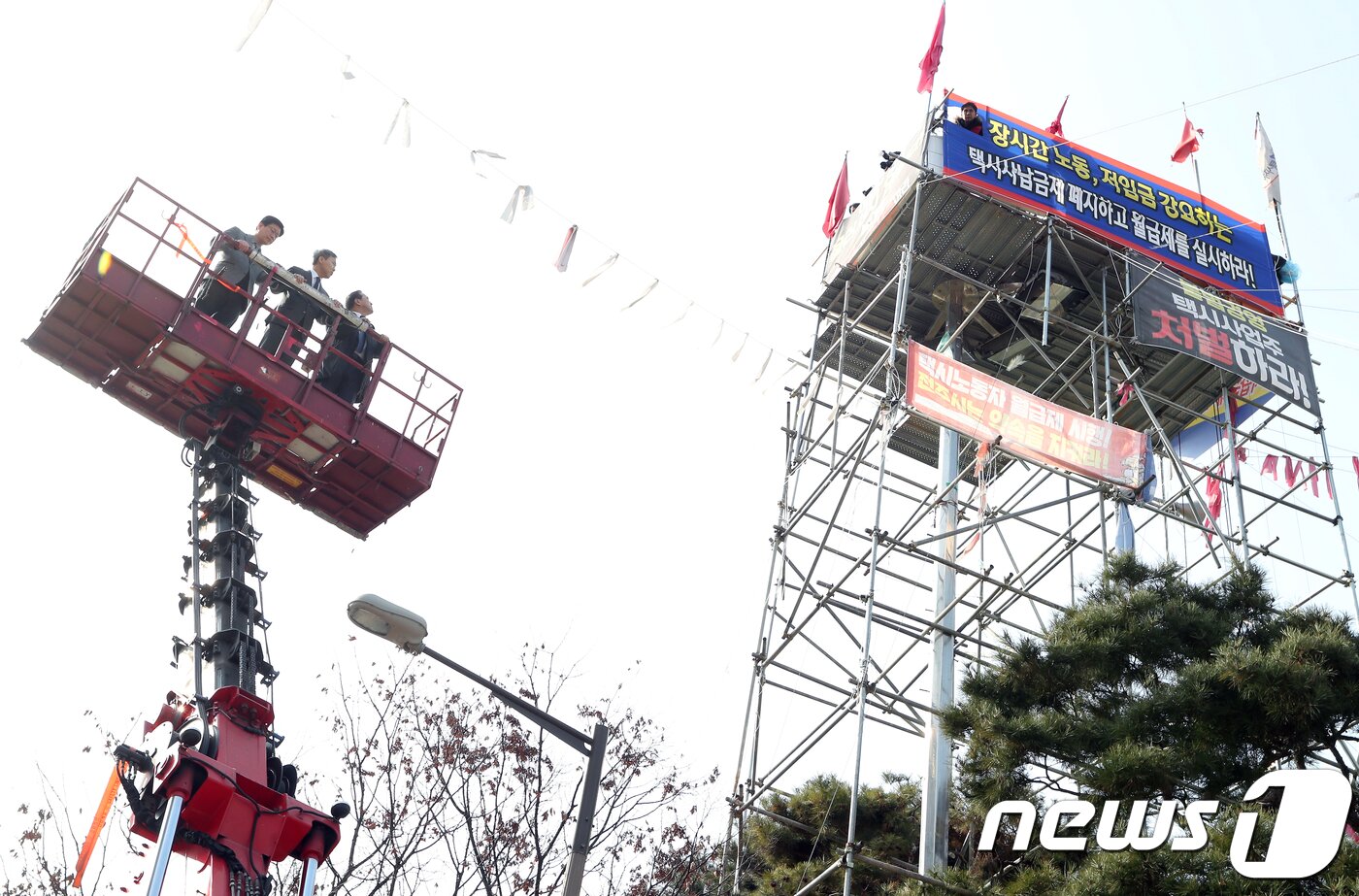 본문 이미지 - 박홍근 더불어민주당 을지키기위원회 위원장과 김승수 전주시장, 안호영 더불어민주당 전북도당위원장이 11일 전북 전주시 전주시청 광장 조명탑에 설치된 김재주씨의 고공농성장을 크레인을 이용해 방문하고 있다. 사납금제도 철폐와 택시전액관리제 도입 등을 주장하며 2017년 9월 4일 고공농성을 시작한 김재주씨는이날로 농성 495일이 되며 16일 500일을 맞는다.2019.1.11/뉴스1 ⓒ News1 문요한 기자