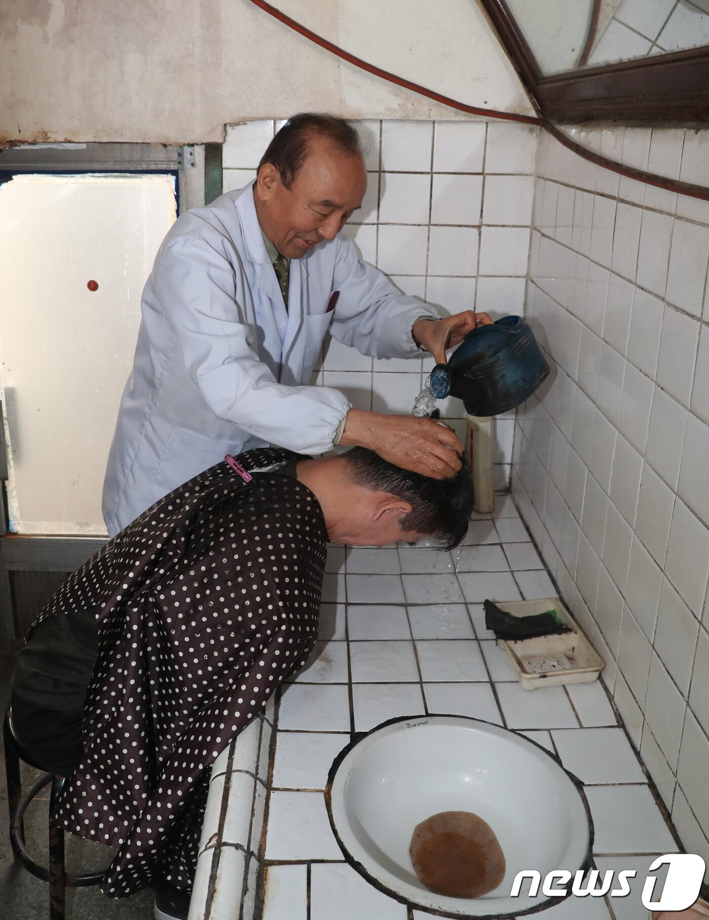본문 이미지 - 대전 동구 소제동 문을 연지 50여년 된 대창미용원 이종완 이발사(82)가 이발을 마친 손님의 머리를 감고 있다. 이 씨는 “10여 년 전부터 재개발 얘기가 나와서 개발이 시작되면 나도 가위를 놓아야지 싶었다. 그렇게 하루하루 기다리다 보니 어느덧 80이 넘어서도 가위를 놓지 못하고 있다”고 말했다. 2019.1.4/뉴스1 ⓒ News1 주기철 기자