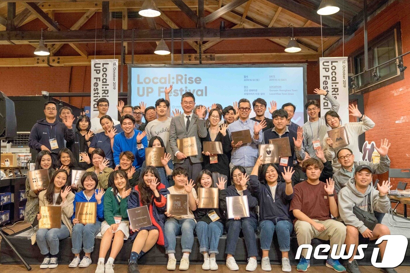 본문 이미지 - 지난 12일 군산 영화동에서 열린 '로컬라이즈 UP 페스티벌'에서 이번 프로젝트에 참가 중인 23개 소셜 벤처 기업인들이 현판을 전달 받고 환하게 웃고 있다.ⓒ 뉴스1