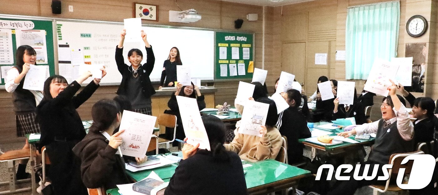 본문 이미지 - 7일 오전 '한 학기 한 권 읽기' 국어수업을 받고 있는 제주대학교사범대학부설중학교 2학년 6반 학생들이 직접 꾸민 '서평쓰기' 수행평가지를 들어 보이며 활짝 웃고 있다. 2019.11.7 /뉴스1 ⓒ News1