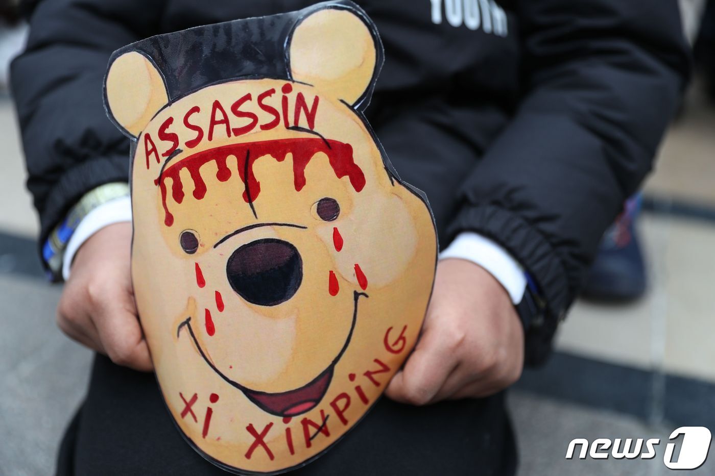 본문 이미지 - 시진핑 중국 국가주석을 닮았다는 이유로 당국의 검열을 받는 곰돌이 푸. 시 주석의 프랑스 방문에 항의하는 시위가 열린 지난해 3월24일(현지시간) 한 시위 참가자가 '시진핑은 살인자'라는 문구가 적힌 푸 가면을 들고 있다. ⓒ AFP=뉴스1