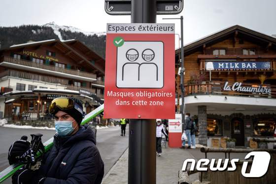 지난 21일 스위스 남부 발레주의 스키 휴양지 베흐비에에서 한 관광객이 코로나19 예방을 위한 마스크 착용 권고 표지판 옆에 서 있다. © AFP=뉴스1