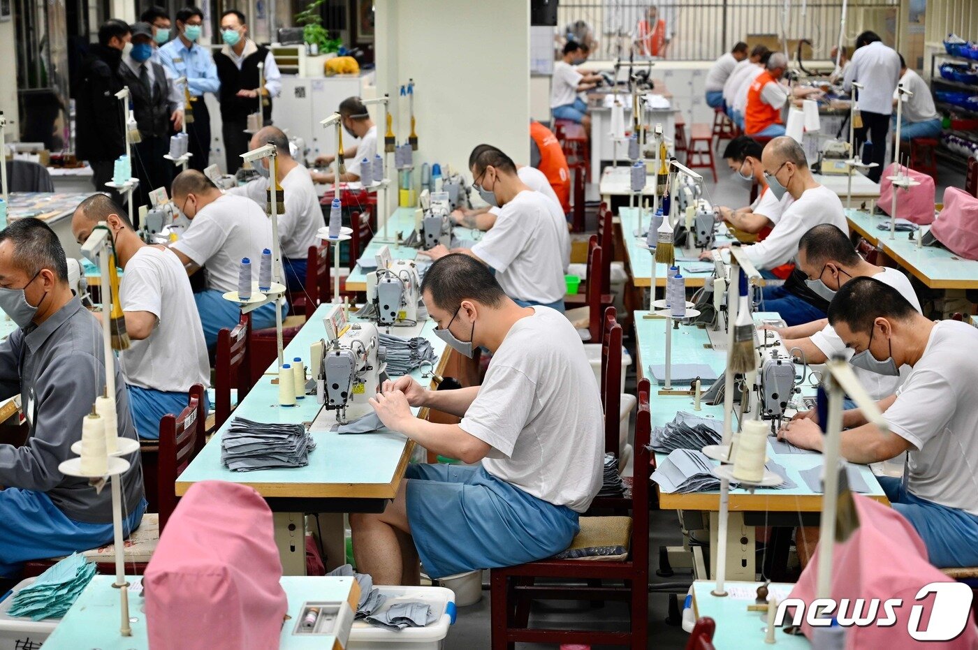 본문 이미지 - 반팔 티셔츠에 반바지 차림으로 부지런히 마스크를 만드는 재소자들. 왼쪽 뒤편으로 이들을 감독하는 교정관 모습도 보인다. ⓒ AFP=뉴스1