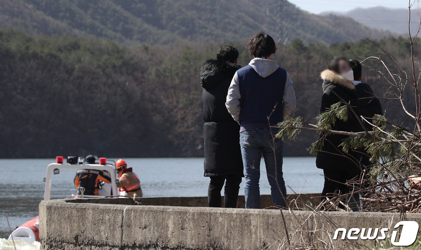 본문 이미지 - 20일 오전 울산 울주군 회야저수지에서 소방대원들이 전날 발생한 산불 진화작업 중 헬기가 추락해 실종된 부기장을 찾기 위해 수색 작업을 벌이고 있는 가운데 유가족들이 사고현장을 바라보고 있다. 2020.3.20/뉴스1 ⓒ News1 윤일지 기자