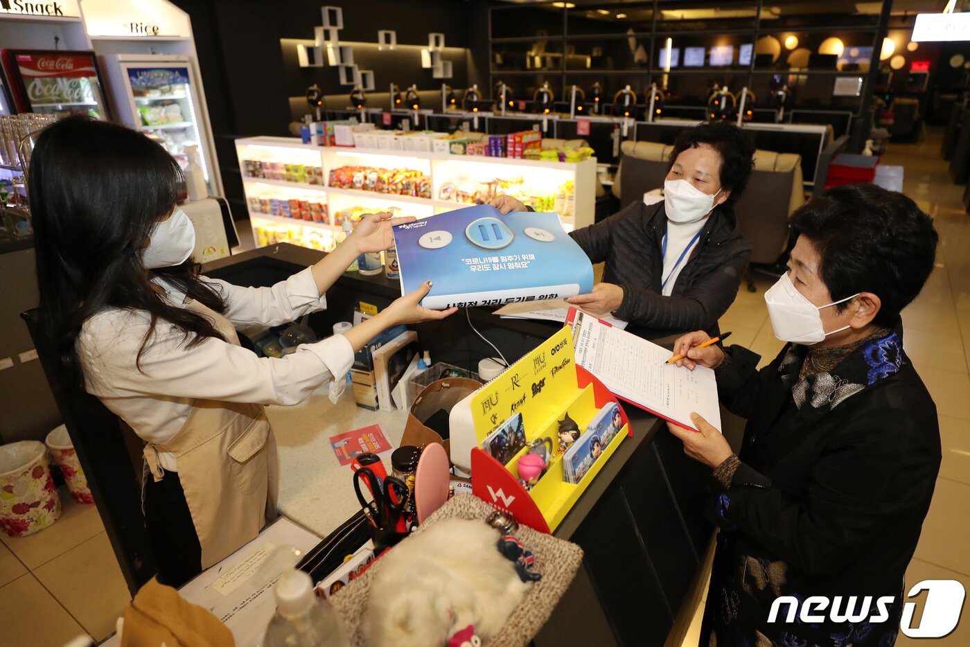 본문 이미지 - 광주 광산구 송정2동 한 PC방에서 '집단감염 위험시설 민관점검반' 관계자들이 '코로나19를 멈추기 위해 우리도 잠시 멈춰요'라고 적힌 사회적 거리 두기 홍보물을 나눠주고 있다. 뉴스1DB