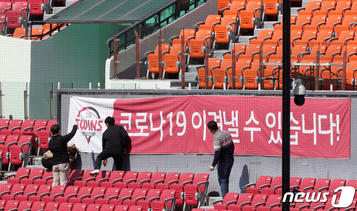 본문 이미지 - 14일 오후 서울 송파구 잠실야구장에서 프로야구 LG트윈스 관계자들이 응원단석 앞에 '코로나19 이겨낼 수 있습니다' 문구가 적힌 현수막을 걸고 있다. 한편, 이날 한국야구위원회(KBO)는 긴급이사회를 열고 10개 프로야구단 사장들과 신종 코로나바이러스 감염증(코로나19)로 연기된 시즌 개막 및 주요 사안을 논의했다. 2020.4.14 ⓒ 뉴스1 이동해 기자
