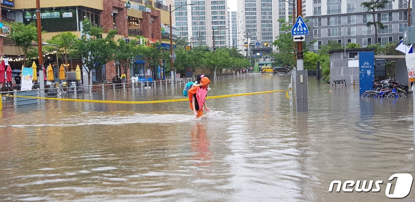 본문 이미지 - 10일 오전 호우경보가 내린 부산 연제구 연산동의 한 아파트 앞 도로가 침수하자 소방대원이 초등학생을 업고 구조하고 있다. (부산소방본부 제공). 2020.7.10/뉴스1 ⓒ News1