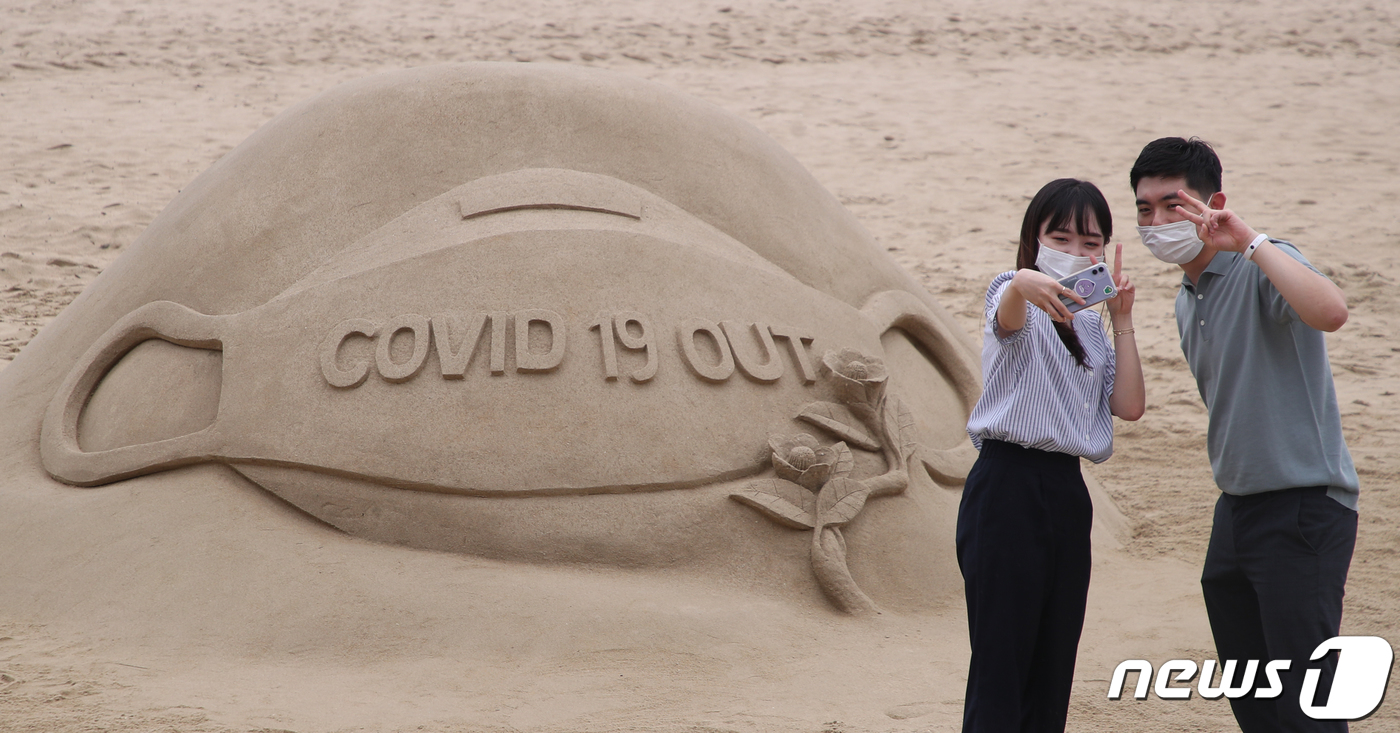 (부산=뉴스1) 여주연 기자 = 22일 오후 부산 해운대해수욕장에서 코로나 바이러스 감염증(코로나 19)예방을 위해 마스크 착용을 독려하는 모래 조각 앞에서 시민들이 기념촬영을 하 …