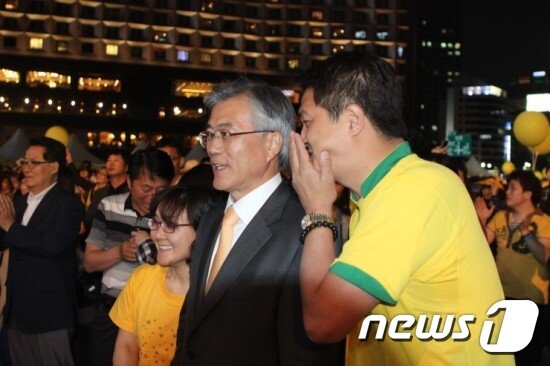 본문 이미지 - 이혁진 전 옵티머스 대표가 지난 2012년 서울시청 광장에서 열린 故(고) 노무현 전 대통령 3주기 추모공연 현장에서 문재인 대통령에게 귓속말을 하고 있다.(출처=이혁진 전 대표 블로그) ⓒ 뉴스1