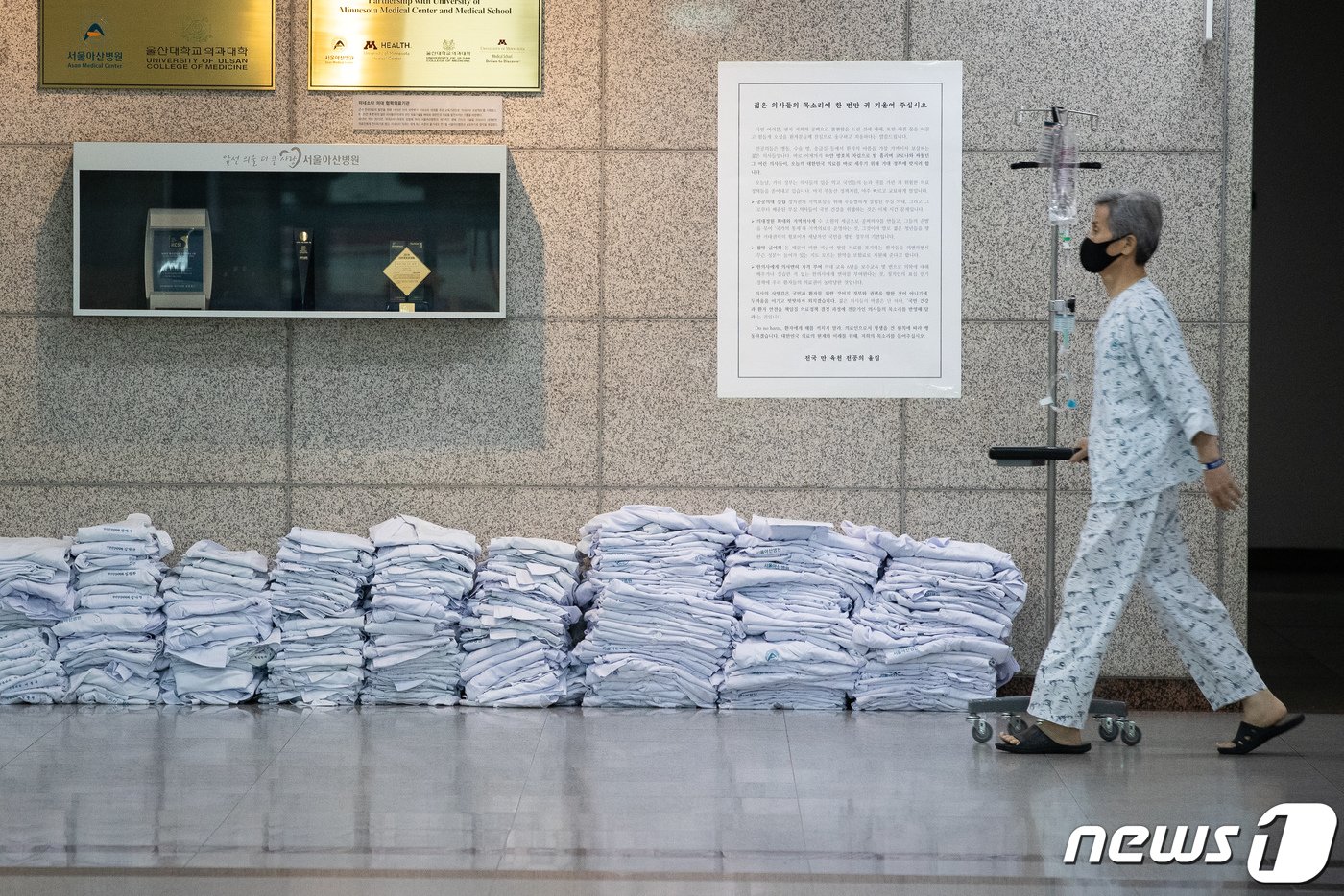 23일 서울 송파구 서울아산병원 로비에 전공의들이 벗어놓은 의사 가운 앞으로 한 환자가 지나가고 있다. 정부의 의과대학 정원 확대 등에 반대하는 대한전공의협의회는 이날 전국 수련병원에서 담화문을 발표하고 의사 가운을 벗는 퍼포먼스를 펼친 후 무기한 파업에 들어갔다. 2020.8.23/뉴스1 ⓒ News1 유승관 기자