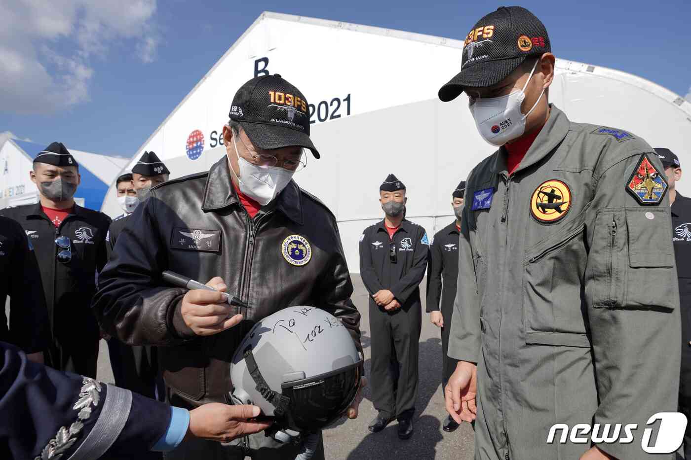 문재인 대통령이 20일 경기도 성남시 서울공항에서 열린 2021 서울 국제 항공우주 및 방위산업 전시회(ADEX) 개막 기념행사에 참석해 시범비행을 마친 공군 특수비행팀 블랙이글스 대원들과 인사하며 FA-50 비행시 착용한 헬멧에 사인을 하고 있다. 이광호 기자