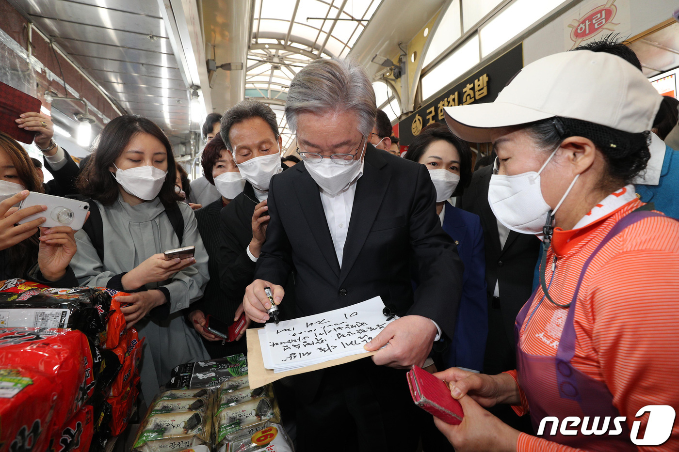 (서울=뉴스1) 국회사진취재단 = 이재명 더불어민주당 대선 후보가 27일 오전 서울 관악구 신원시장을 방문, 한 상인에게 ‘함께 사는 세상’이란 방명록과 사인을 해주고 있다. 20 …