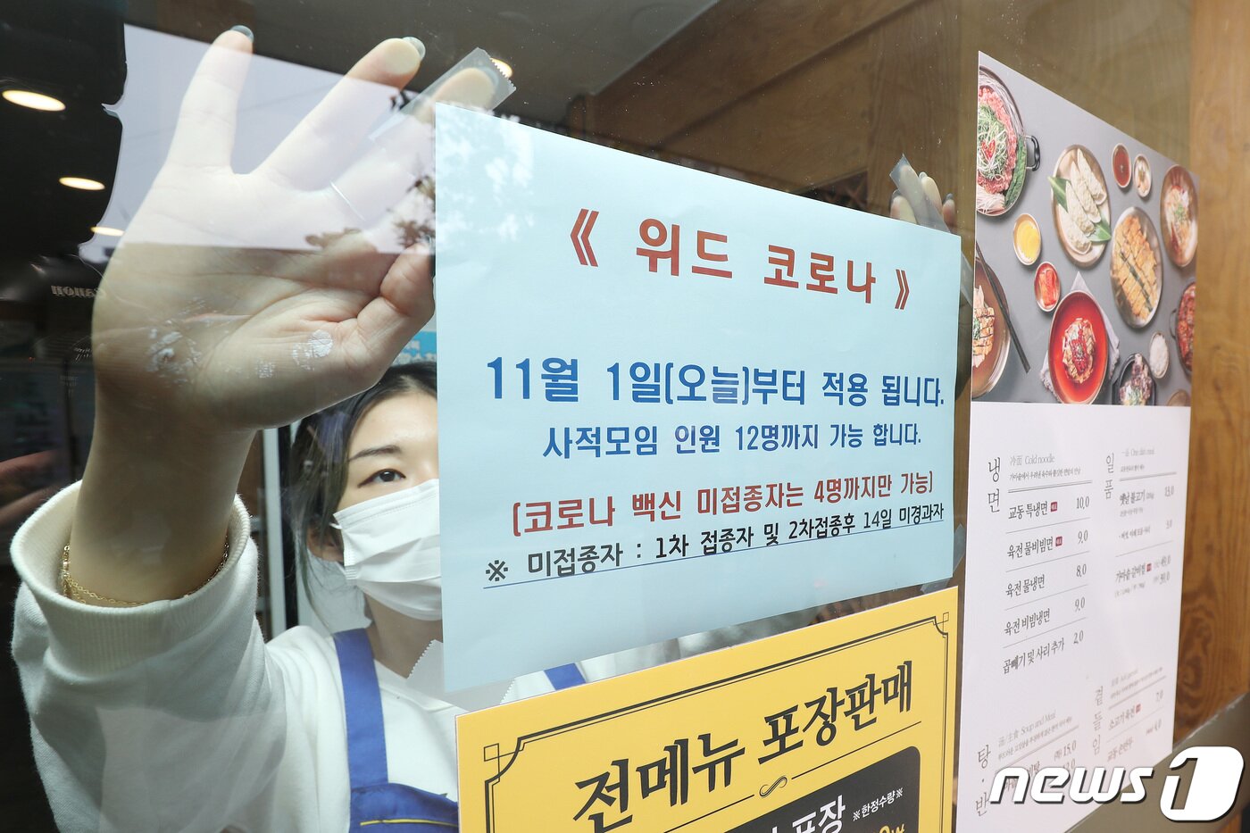 본문 이미지 - 단계적 일상회복(위드 코로나) 시행 첫날인 1일 대구 중구의 한 음식점 관계자가 점심시간을 앞두고 유리창에 최대 12명 모임 가능 안내문을 붙이고 있다. 2021.11.1/뉴스1 ⓒ News1 공정식 기자