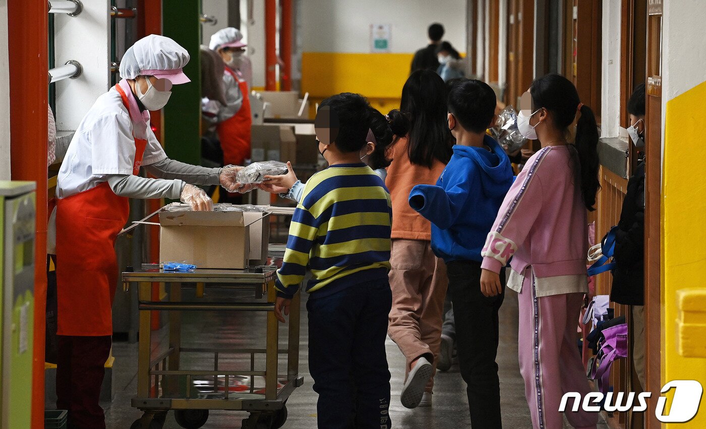 본문 이미지 - 급식 노동자, 돌봄 전담사, 방과 후 강사 등 학교 비정규직 노동자들로 구성된 전국학교비정규직연대회의가 총파업에 돌입한 2일 서울 시내 한 초등학교 학생들이 구청에서 파견된 어르신들게 복도에서 빵과 쿠키 등으로 구성된 대체식을 배식받고 있다. 2021.12.2/뉴스1 ⓒ News1 박정호 기자