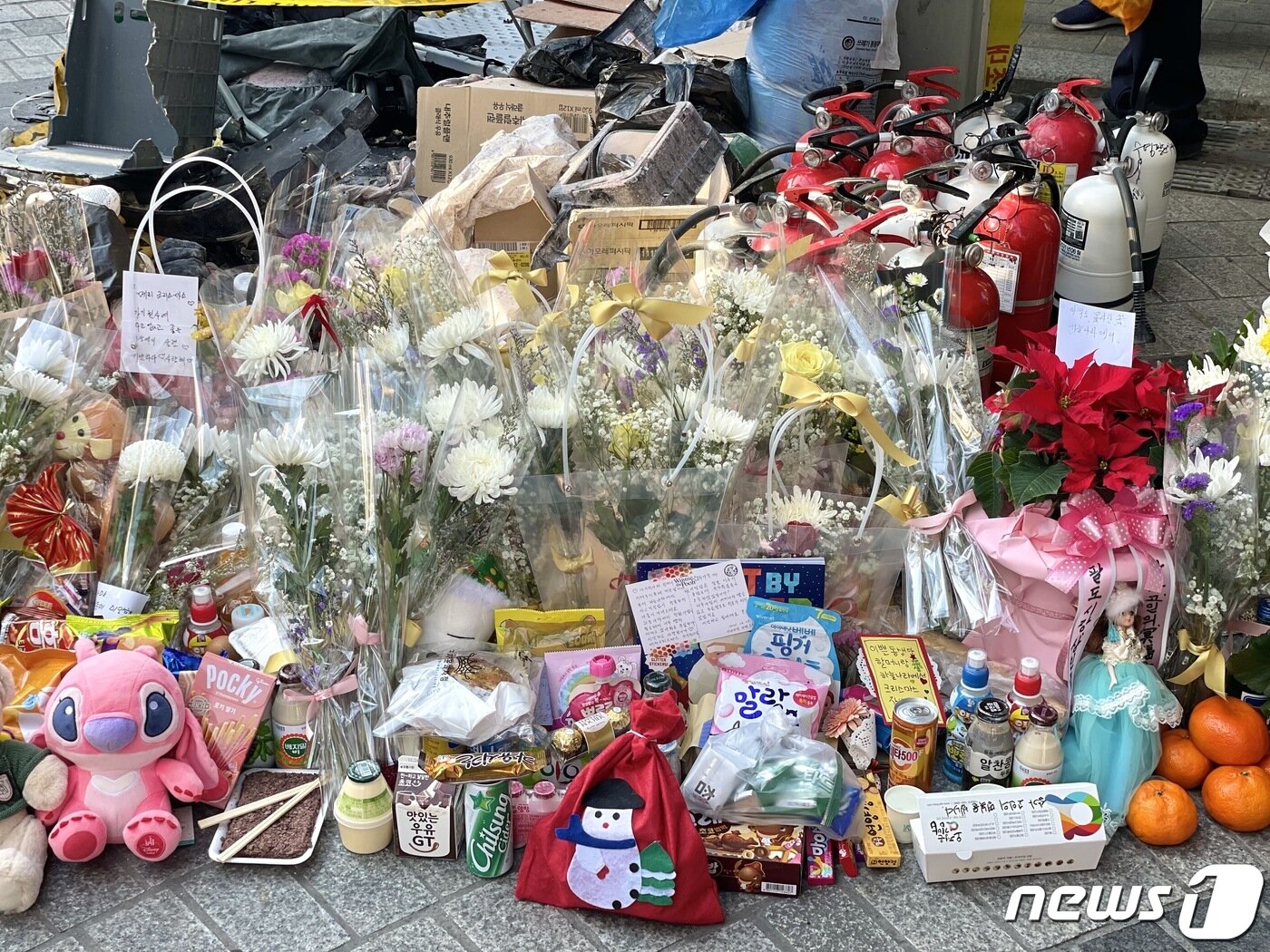 본문 이미지 - 지난해 12월23일 오후 부산 수영구 수영팔도시장 입구에 교통사고 희생자를 추모하는 꽃다발, 편지, 간식, 소화기 등 추모물품이 쌓여 있다.2021.12.23/ ⓒ 뉴스1 이유진 기자
