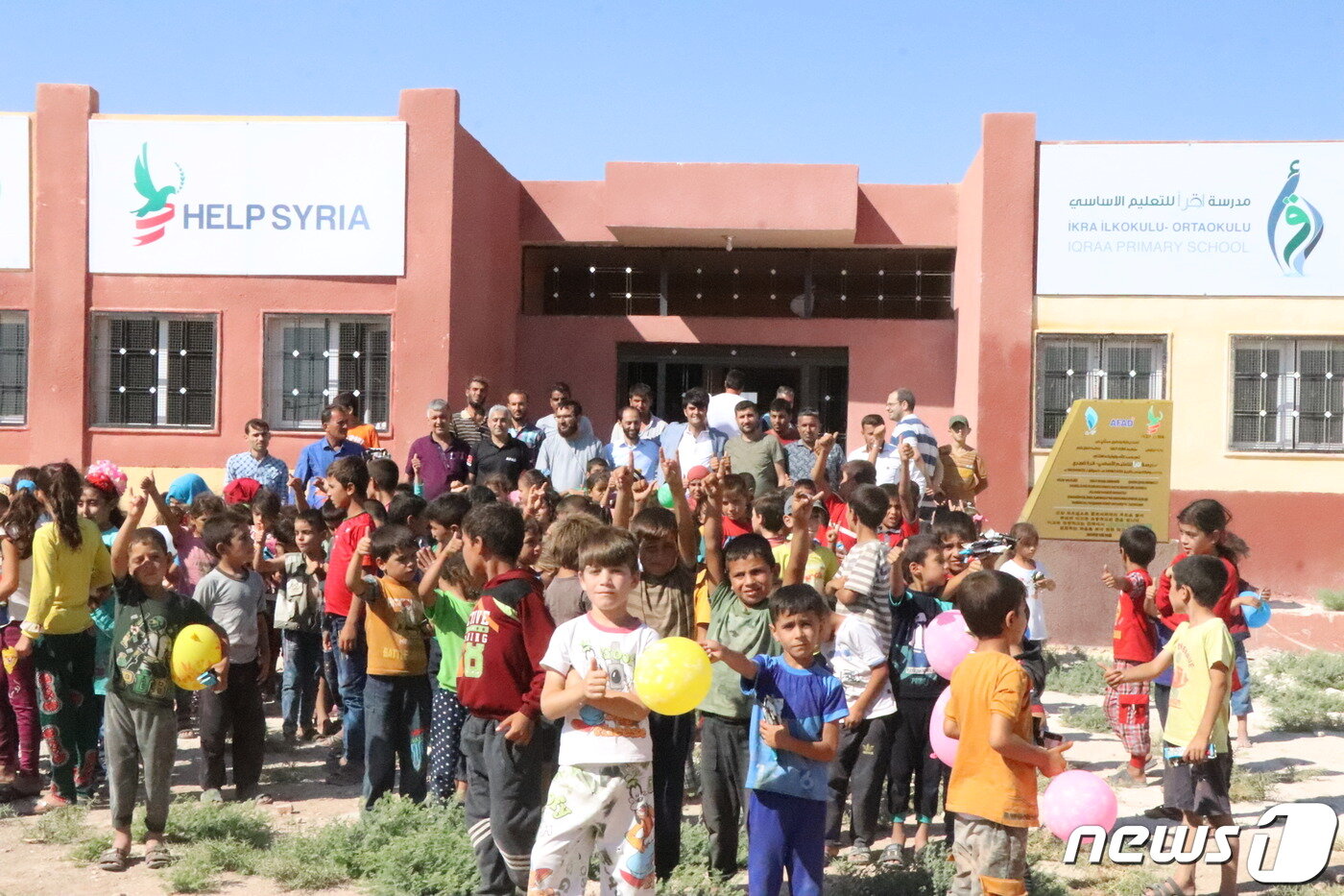본문 이미지 - 지난 2019년 8월 시리아 알레포에 건립된 '이끄라 초등학교'앞에서 공사에 참여한 단체 관계자들과 학교 학생들이 모여있다.(헬프시리아 제공) ⓒ 뉴스1