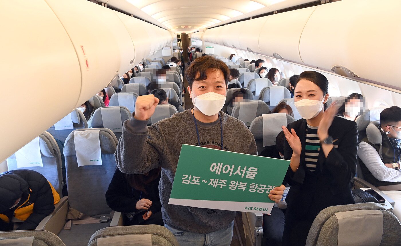 본문 이미지 - 에어서울 무착륙 관광비행 기내 이벤트에서 우승한 탑승객이 김포~제주 왕복항공권을 받고 캐빈승무원과 기념 촬영을 하고 있다