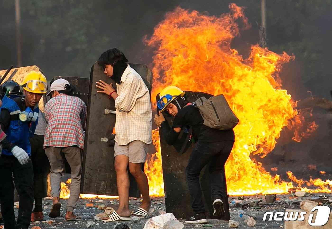 2021년 3월16일(현지시간) 미얀마 양곤에서 군사 쿠데타를 규탄하는 시위대가 경찰과 충돌을 하며 직접 만든 방패 뒤에서 화염을 피하고 있다. © AFP=뉴스1 © News1 우동명 기자