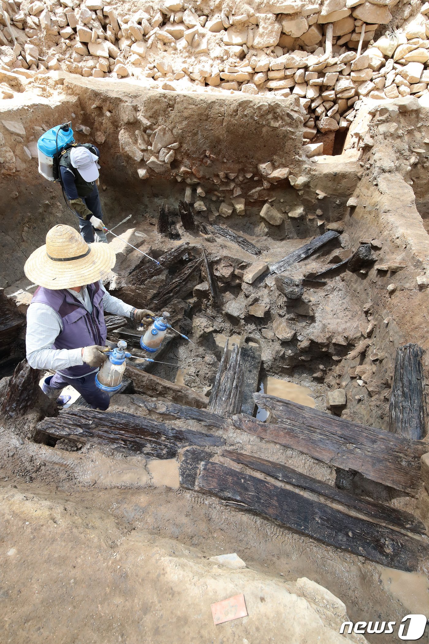 본문 이미지 - 지난 2021년 4월28일 대구 북구 노곡동 함지산 팔거산성에서 화랑문화재연구원 관계자들이 7세기 초반 신라시대 목간(木簡·문서나 편지 등의 글을 일정한 모양으로 깎아 만든 나무 또는 대나무 조각에 적은 것)이 출토된 집수지 주변 발굴 현장에서 수분을 유지하기 위해 목재에 물을 뿌려 관리하고 있다. 2021.4.28/뉴스1 ⓒ News1 공정식 기자