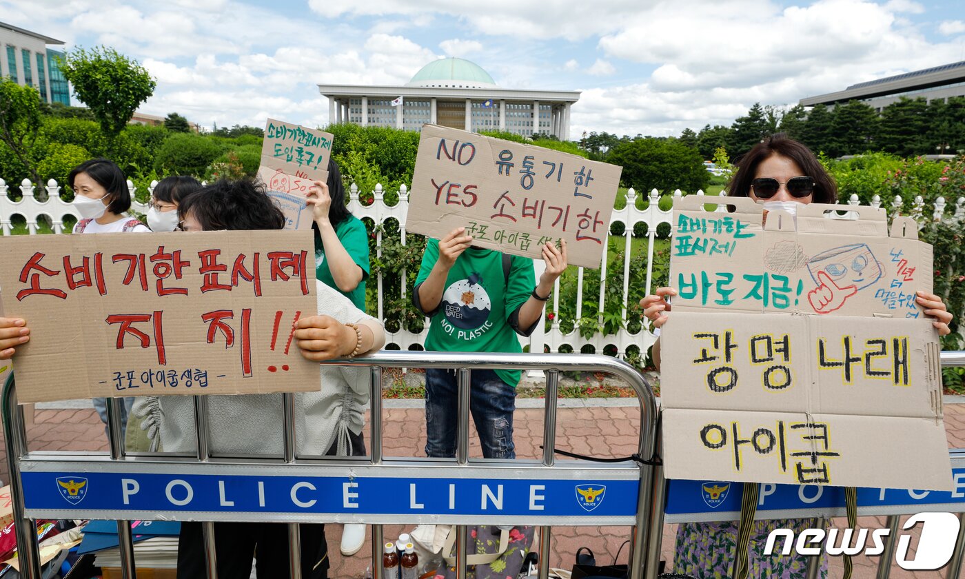 본문 이미지 - 소비자기후행동 회원들이 16일 서울 여의도 국회의사당 앞에서 열린 소비기한표시제 도입 촉구 기자회견에서 폐지로 만든 팻말을 들고 있다. 참가자들은 소비기한표시제가 소비자에게 식품 폐기 시점에 대한 정확한 정보를 전달하고 식품 낭비를 줄여 환경보호를 할 수 있다며 제도 도입을 촉구했다. 2021.6.16/뉴스1 ⓒ News1 안은나 기자