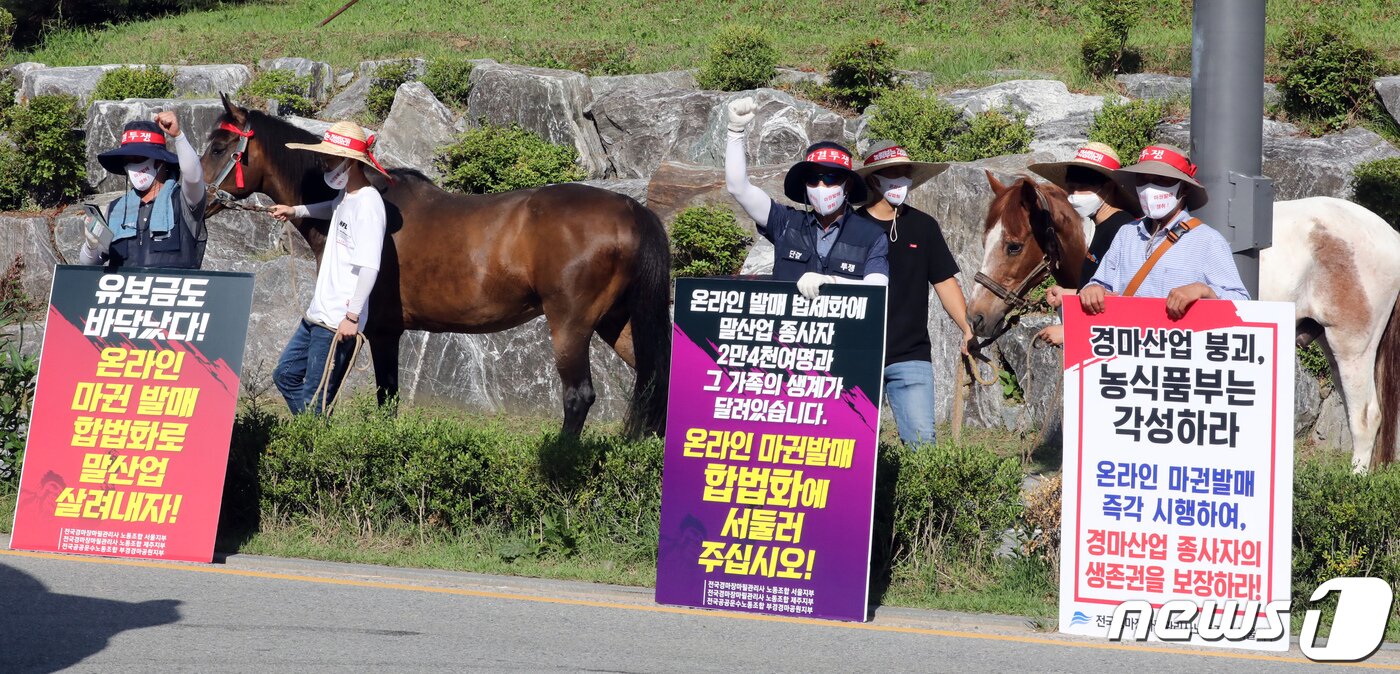 본문 이미지 - 전국경마장마필관리사노동조합 조합원들이 13일 정부세종청사 농림축산식품부에서 말산업 종사자 생존권 보장을 촉구하며 경주마를 끌고 집회 하고 있다. 노조는 코로나19로 인해 경마가 정상적으로 이뤄지지 않음에 따라 온라인 마권 발매 입법화 등 생존 대책을 촉구했다. 2021.7.13/뉴스1 ⓒ News1 장수영 기자