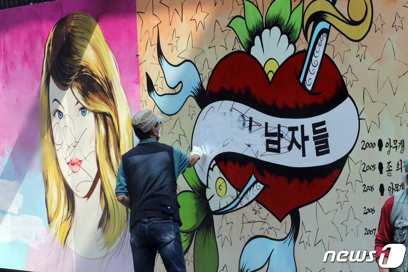 본문 이미지 - 30일 오전 서울 종로구의 한 서점 벽면에 그려진 윤석열 전 검찰총장의 배우자 김건희 씨를 비방하는 내용의 벽화 문구를 서점 관계자가 페인트로 지우고 있다. 2021.7.30/뉴스1 ⓒ News1 황기선 기자