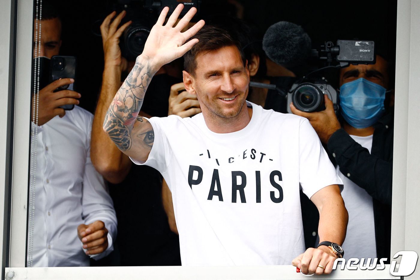 본문 이미지 - 프랑스 프로축구 파리 생제르맹&#40;PSG&#41;과 계약을 앞둔 리오넬 메시가 지난 10일&#40;현지시간&#41; 파리 인근 르부르제 공항 창가에서 &#39;여기는 파리입니다&#39; 라는 PSG 슬로건이 적힌 흰색 티셔츠를 입고 팬들을 향해 손을 흔들고 있다. ⓒ AFP=뉴스1