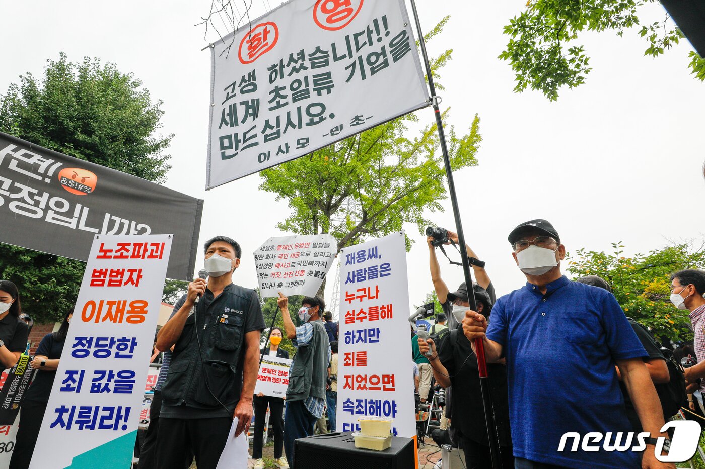 본문 이미지 - 정주교 전국금속노동조합 부위원장이 13일 오전 경기 의왕 서울구치소 앞에서 열린 &#39;이재용 특혜 가석방 규탄 기자회견&#39;에서 발언하는 중 이 부회장의 가석방을 환영하는 시민이 옆에 깃발을 들고 서 있다. ⓒ News1 안은나 기자