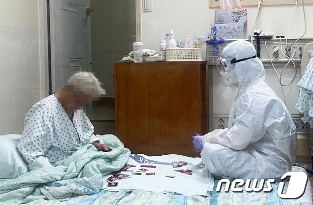 본문 이미지 - 신종 코로나바이러스 감염증(코로나19)에 확진돼 음압병동에 홀로 격리된 할머니와 방호복을 입은 간호사가 화투로 그림을 맞추는 모습이 담긴 사진이 공개됐다. 사진 속 방호복을 입은 의료진은 삼육서울병원 간호사 이수련(29)씨이다. 3일 대한간호협회는 이 사진에 대해 "올해 공모한 제2차 간호사 현장 수기·사진전에 출품된 작품＂이라고 밝혔다. (대한간호협회 제공)/뉴스1