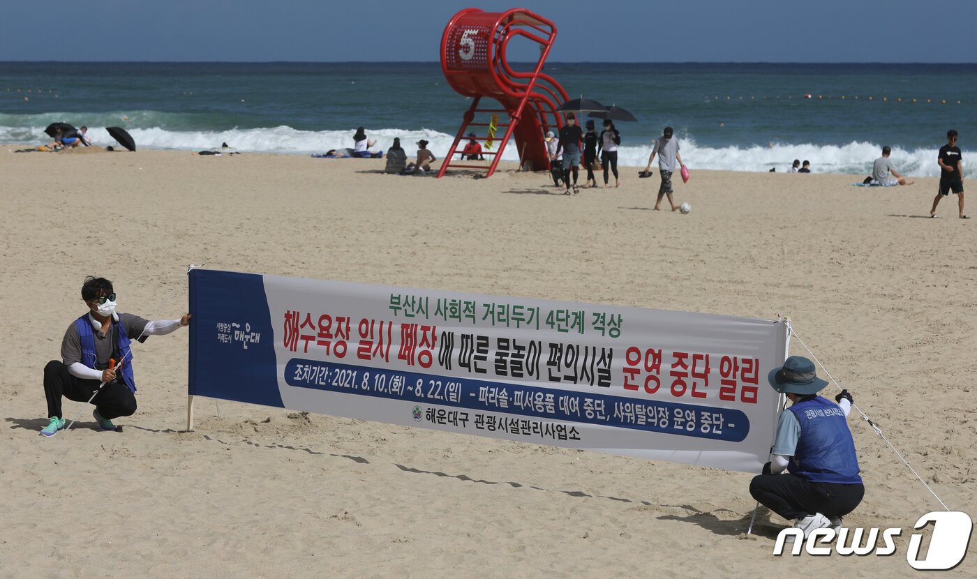 본문 이미지 - 해수욕장 폐쇄를 하루 앞둔 9일 부산 해운대해수욕장 관리사업소 관계자들이 &#39;해수욕장 일시 폐장 물놀이 편의시설 운영중단&#39; 안내 현수막을 백사장에 설치하고 있다. 부산시는 10일 0시부터 사회적 거리두기 단계를 4단계로 격상한다. ⓒ News1 여주연 기자