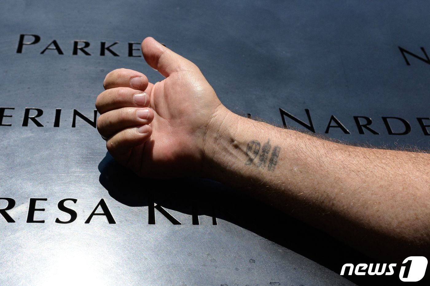 본문 이미지 - 8일(현지시간) 911 테러 생존자인 조셉 디트마르가 세계무역센터 자리에 마련된 911 추모 공원 앞 기념비 위에 '911' 글자를 새긴 자신의 오른 손목을 드러내 보이고 있다. 당시 그는 세계무역센터 105층에서 근무를 하고 있었다. 2021.06.08 ⓒ AFP=뉴스1