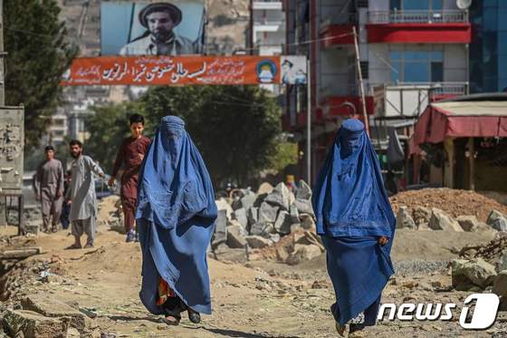 8일 (현지시간) 아프가니스탄의 카불에서 부르카를 입은 여성들이 '국부' 아흐마드 샤 마수드의 사진이 걸린 건물 옆을 지나가고 있다. © AFP=뉴스1 © News1 우동명 기자