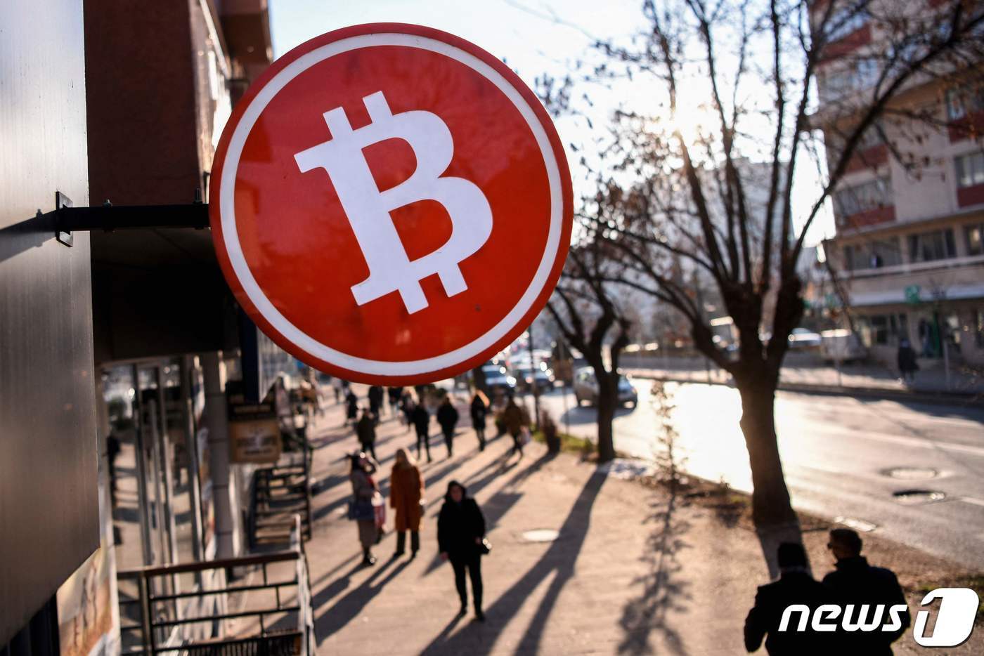 본문 이미지 - 사람들이 2022년 1월 17일(현지시간) 코소보 프리스티나의 한 암호화폐 거래소에 전시된 비트코인 암호화폐 상징물 아래로 걸어가고 있다. ⓒ AFP=뉴스1 ⓒ News1 김지현 기자