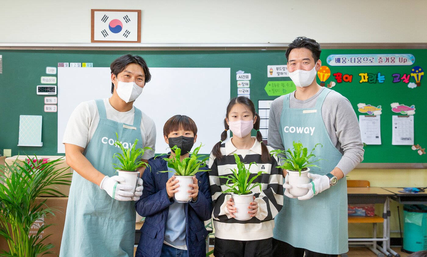 본문 이미지 - 코웨이 임직원 봉사자와 초등학생들이 청정학교 교실숲 식물을 들고 있다.(코웨이 제공) 