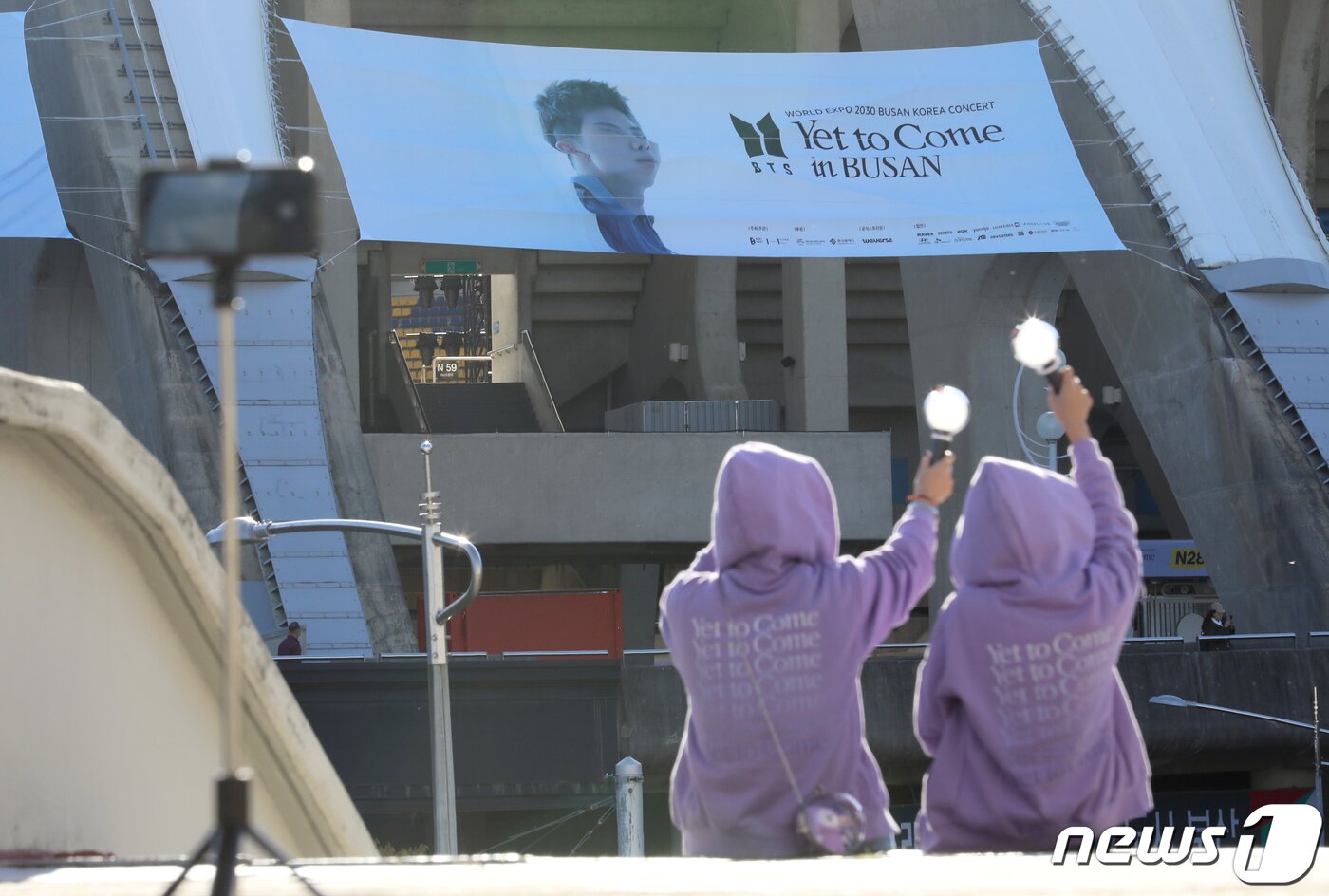 본문 이미지 - 2030 부산세계박람회 유치 기원 BTS콘서트를 이틀 앞둔 13일 부산 연제구 부산아시아드주경기장서 일본 BTS팬들이 BTS멤버 RM 현수막을 배경으로 아미봉으로 인증샷을 찍고 있다. 2022.10.13/뉴스1 ⓒ News1 김영훈 기자