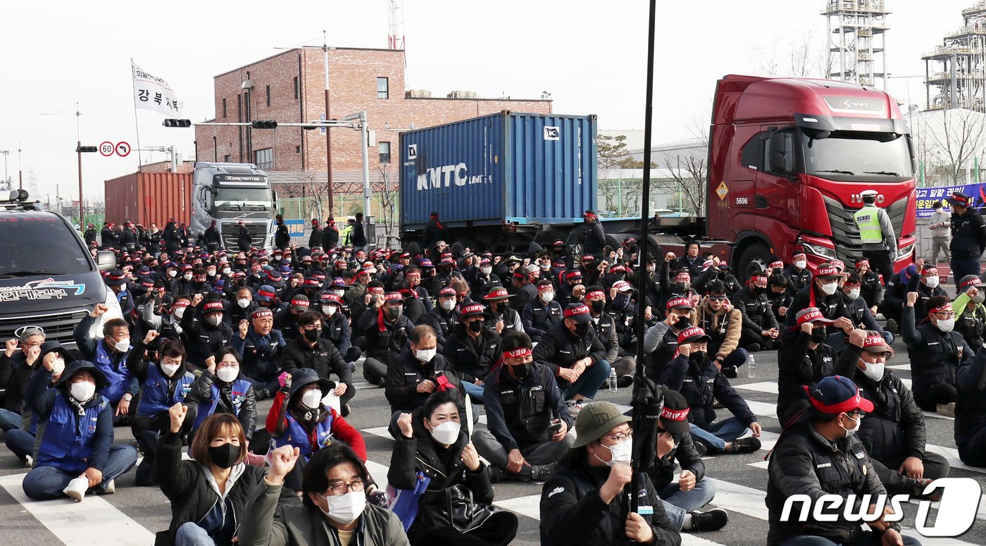 24일 울산 남구 울산신항 앞에서 민주노총 전국공공운수노동조합 화물연대 울산본부 총파업 출정식이 열린 가운데 구호를 외치는 조합원들 뒤로 화물차들이 울산신항으로 들어가고 있다. 화물연대는 △안전운임 일몰제 폐지 △안전운임제 전차종, 전품목으로 확대 △노동기본권 확대·화물노동자 권리보장 등을 요구하고 있다. 2022.11.24/뉴스1 ⓒ News1 윤일지 기자