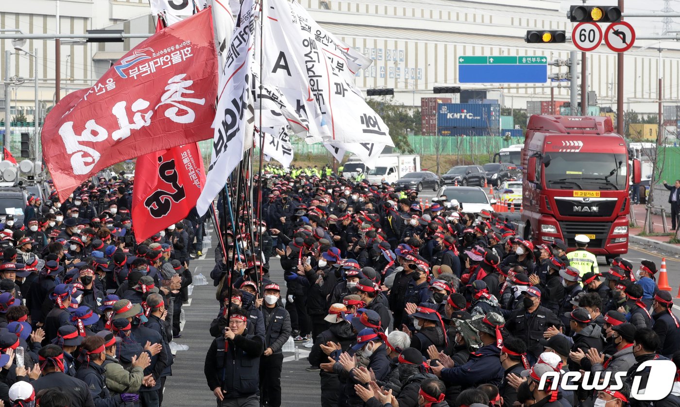 24일 울산 남구 울산신항 앞에서 민주노총 전국공공운수노동조합 화물연대 울산본부 총파업 출정식이 열린 가운데 입장하는 깃발 뒤로 화물차가 지나가고 있다. 2022.11.24/뉴스1 ⓒ News1 윤일지 기자